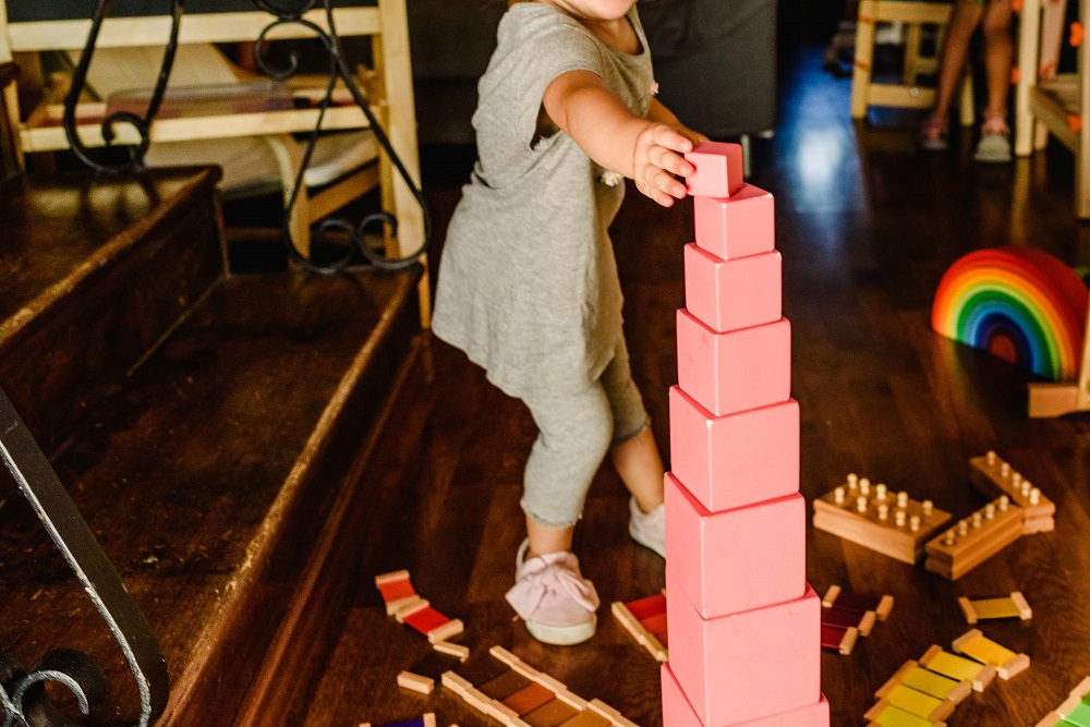 A child carefully building the Pink Tower, a classic Montessori sensorial material